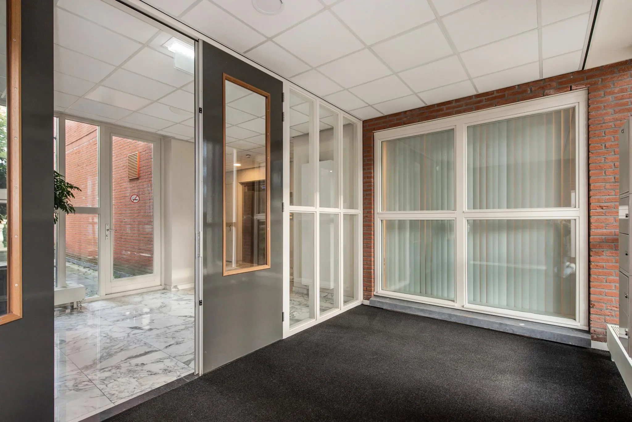 Entreehal van een kantoorpand aan de Laan van Vredenoord met glazen deuren, marmeren vloer en grote ramen met verticale lamellen.